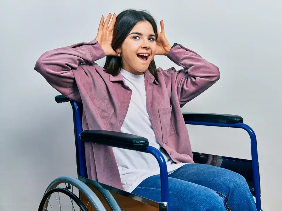 Young woman using a wheelchair smiling with her hands raised.